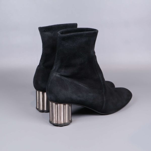 Bakre vy av svarta mockastövletter och cylinderformad klack i metallton
