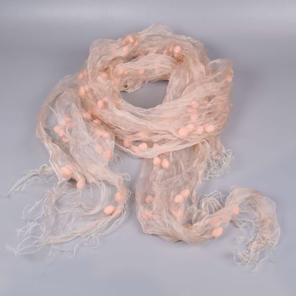 Luftig beige sjal med ljusa pompoms liggande utvecklad