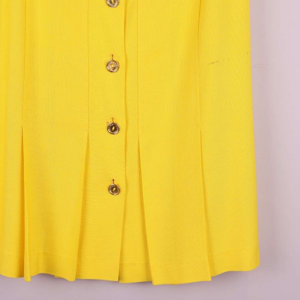 Detaljbild på nederkant och veck fram på gul kjol