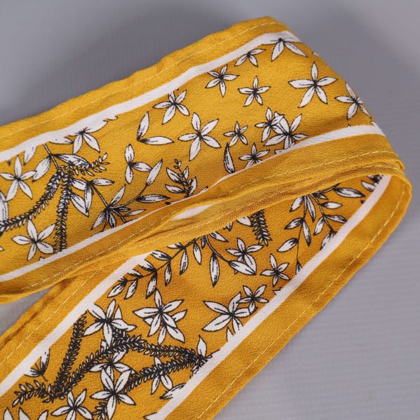 Närbild på gult hårband med vita blommor och vita kanter