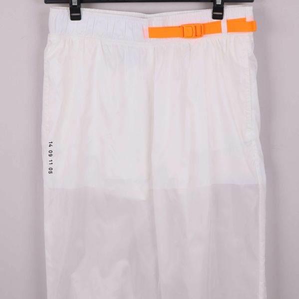 Närbild på orange rem och tryck på vita byxor