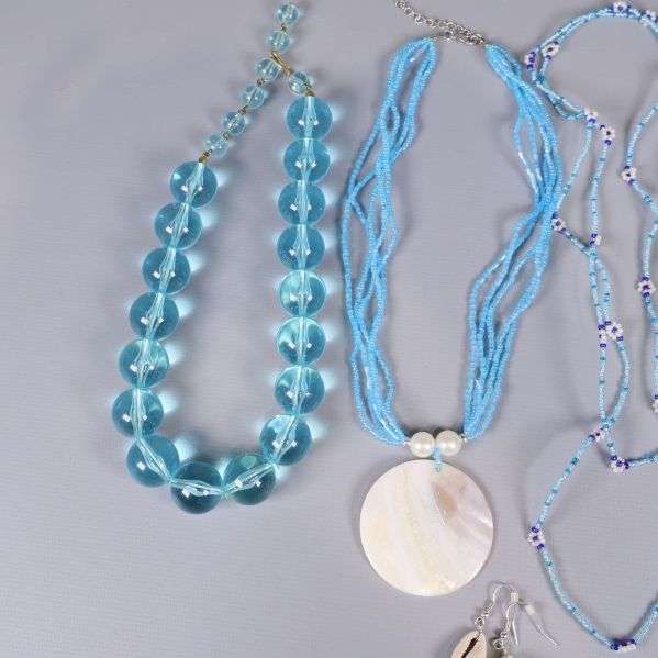 Närbild på blått pärlhalsband och halsband med stor rund snäcka