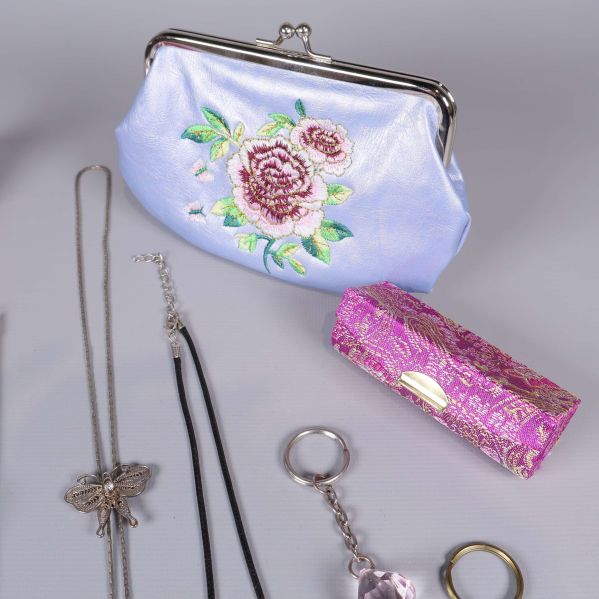 Närbild på ljuslila väska med blombroderi och rosa etui