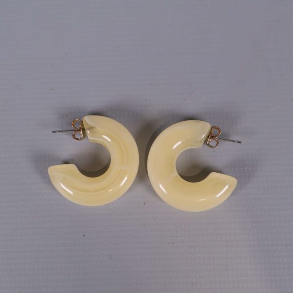 Ett par krämfärgade, blanka örhängen i ringform