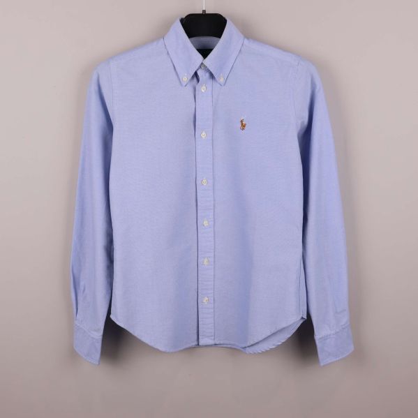 Ljusblå skjorta på galge med knappslå och broderad logga