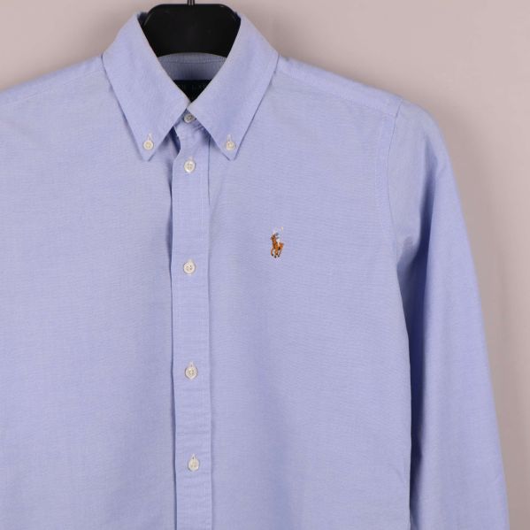 Närbild av broderad logga på skjortans bröst och knappslå