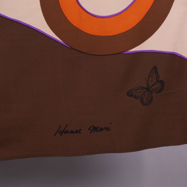 Närbild på signatur och fjäril på brunt tygområde