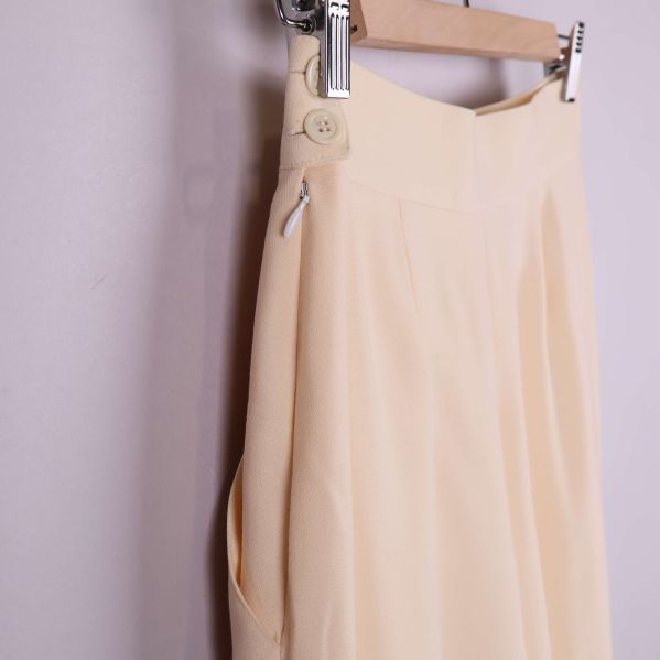 Närbild på midja och knappdetalj på beige byxa