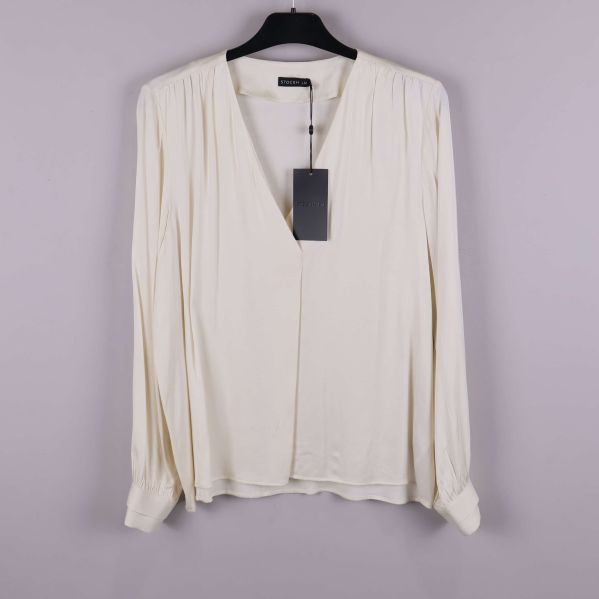 Ljus långärmad blus på galge mot grå bakgrund