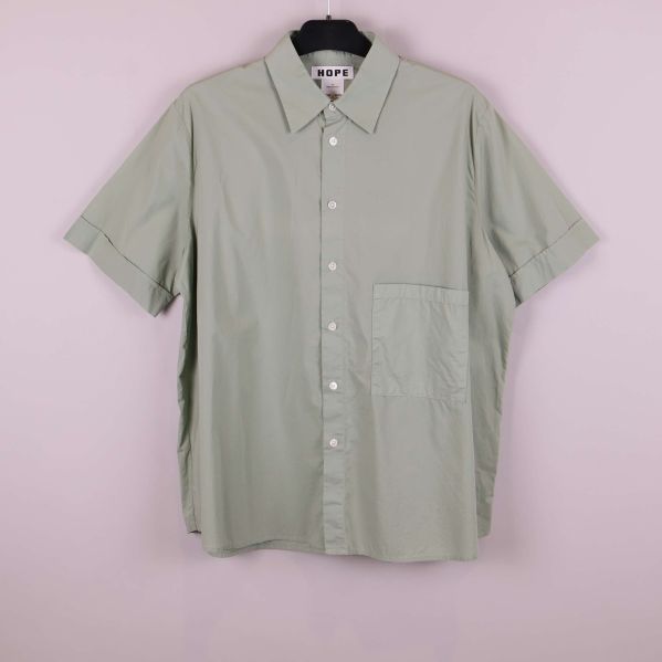 Ljusgrön kortärmad skjorta hänger mot rosa bakgrund