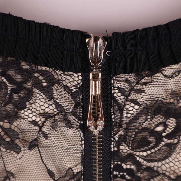 Närbild på guldfärgad dragkedja och spetsdetaljer vid halsringning