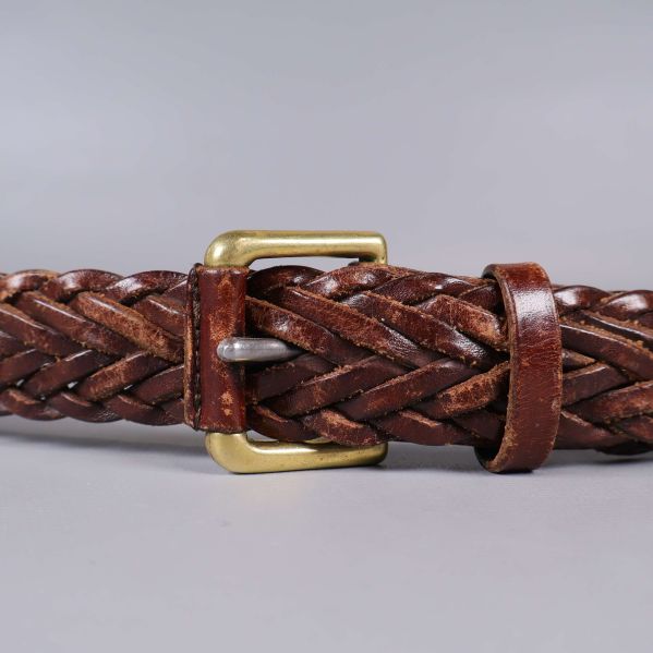 Närbild på bältesspänne i mässing och flätad brun läderrem