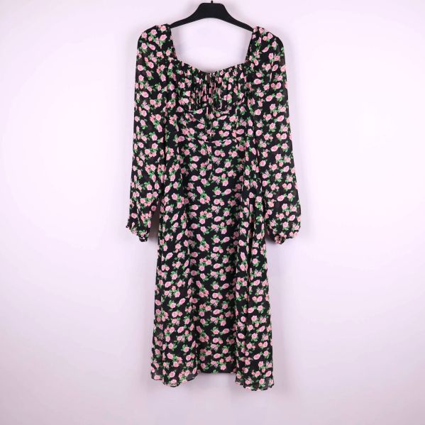 Blommig klänning med långa ärmar upphängd på galge mot ljus bakgrund