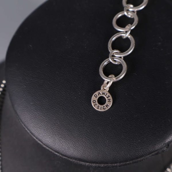 Närbild av märkning Danish Design på halsbandskedjan