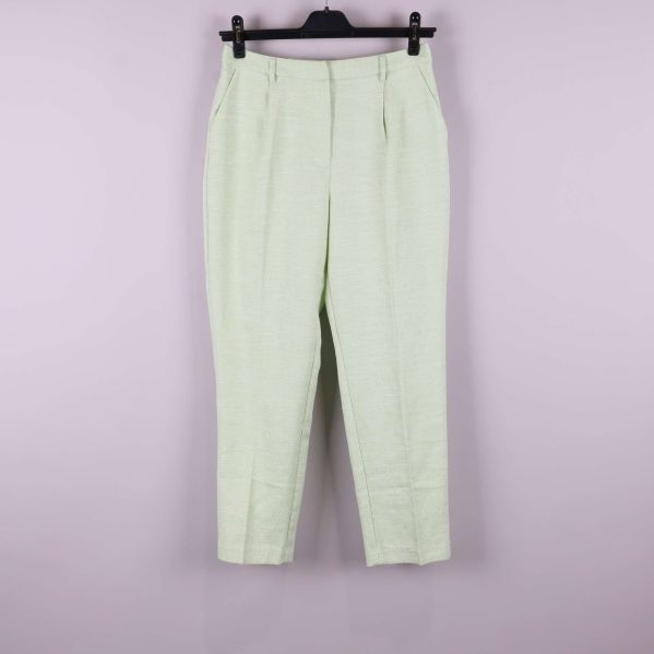 Ljusgröna byxor upphängda mot ljus bakgrund, helbild framifrån