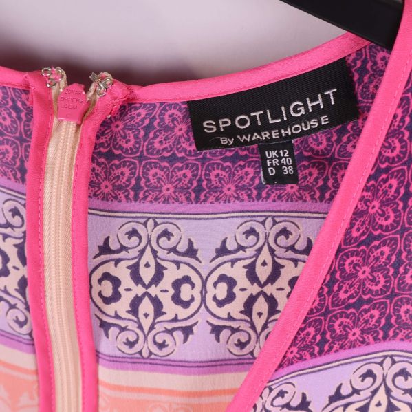 Närbild på klänningsetikett Spotlight by Warehouse med storleksinfo