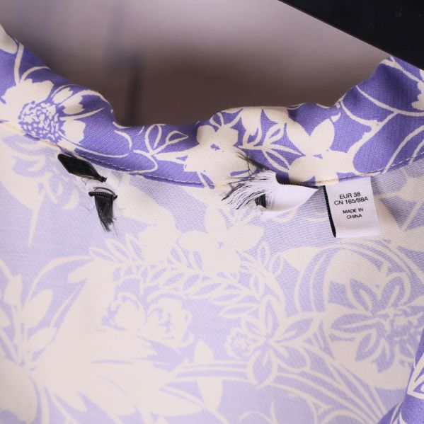 Närbild på krage och etiketter i lila blommig klänning