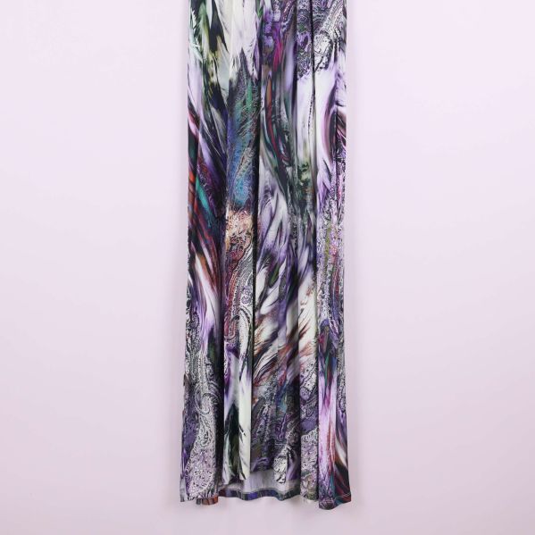 Nederdel av långklänning i flerfärgat tyg mot ljus vägg