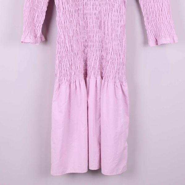 Närbild på nederdelen av ljusrosa smockad klänning