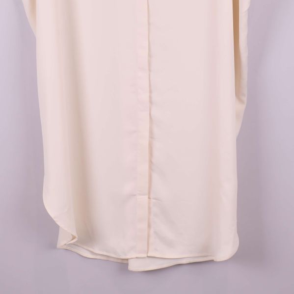 Detalj av nederkant på krämvit kaftan med rundad form