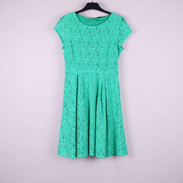Grön spetsklänning med rund hals och korta ärmar hängande på galge, sedd framifrån
