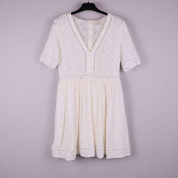 Kort vit klänning med V-ringning och broderade detaljer hängande på galge