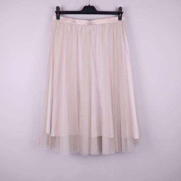 Ljus tyllkjol upphängd mot enfärgad bakgrund framifrån