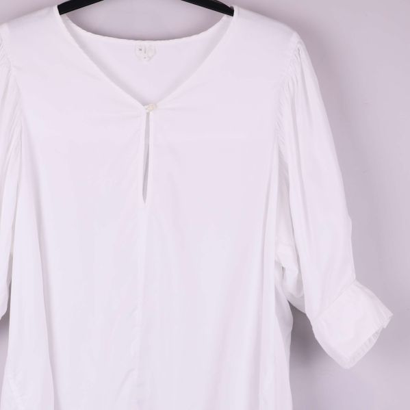 Detaljbild av vit blus med v-ringning och veck