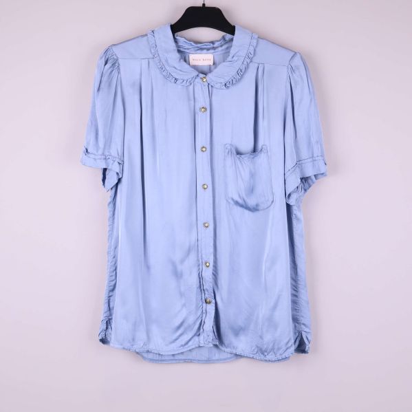 Ljusblå volangblus med kort ärm hängande på galge