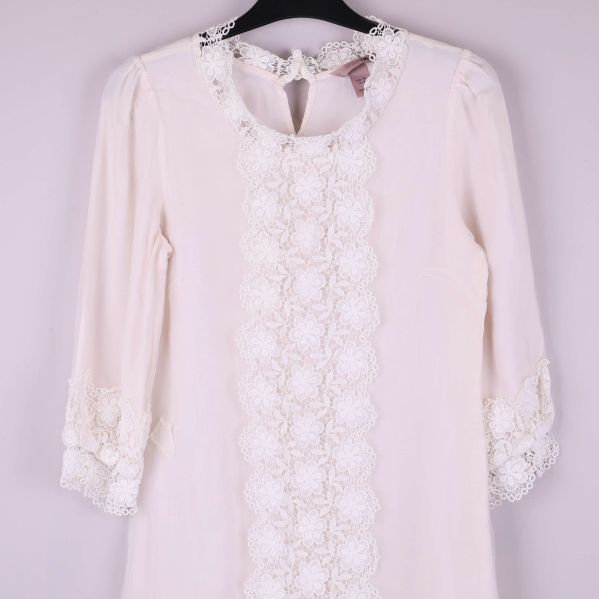 Närbild på klänningens spetsdetaljer framtill vid hals och ärmslut