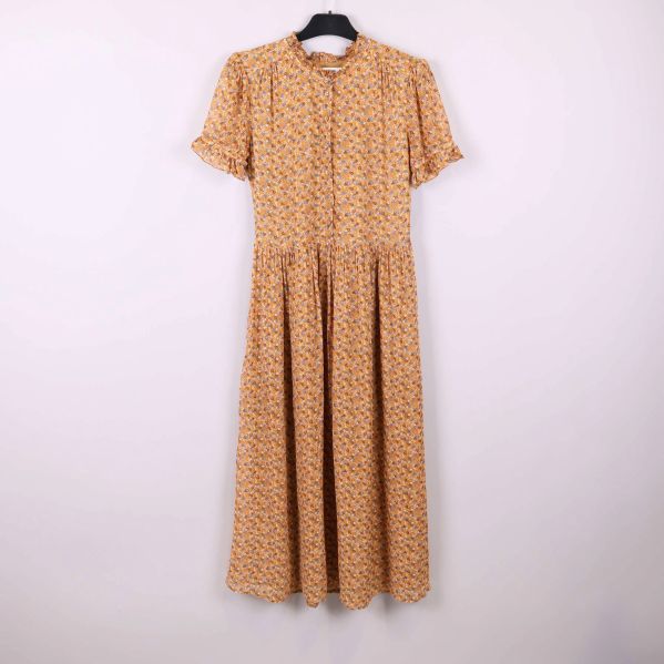 Lång blommig klänning med volanger på galge mot ljus bakgrund