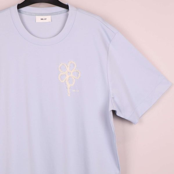 Närbild på broderad vit blomma på t-shirtens vänstra bröst