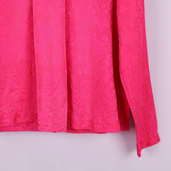 Närbild på nederkant och ärm av cerise mönstrad blus