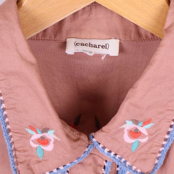 Närbild på krage med blommigt broderi och Cacharel-märke