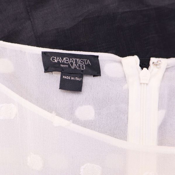 Närbild på Giambattista Valli label och vit dragkedja på toppen