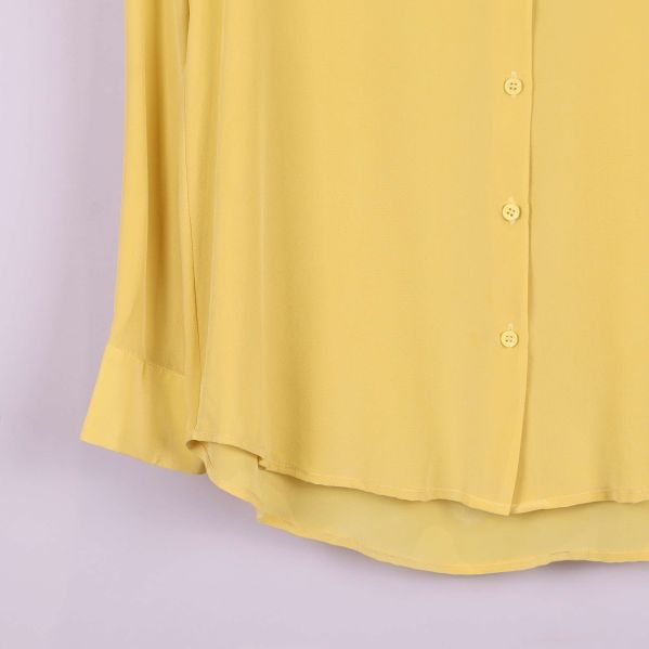 Nedre detalj på framsidan av gul blus med knappslå