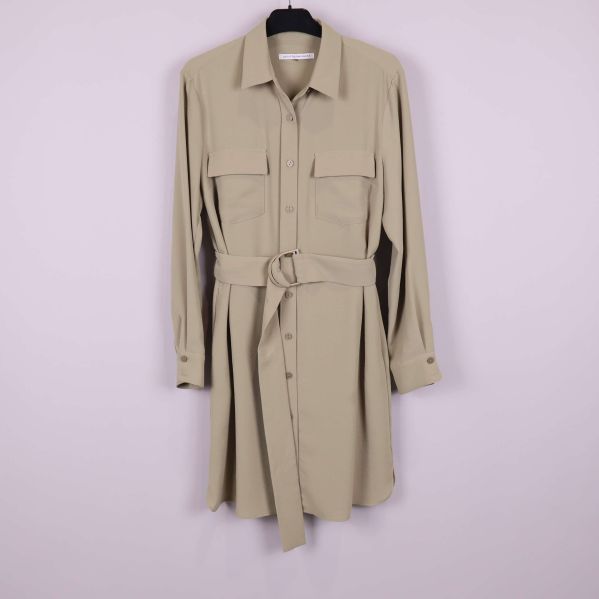 Beige skjortklänning med lång ärm och bälte hängande mot ljus bakgrund