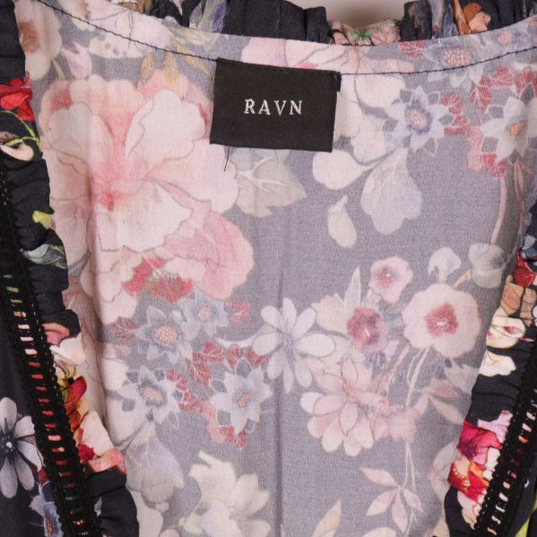 Närbild på klänningens märkning RAVN och blommigt tyg