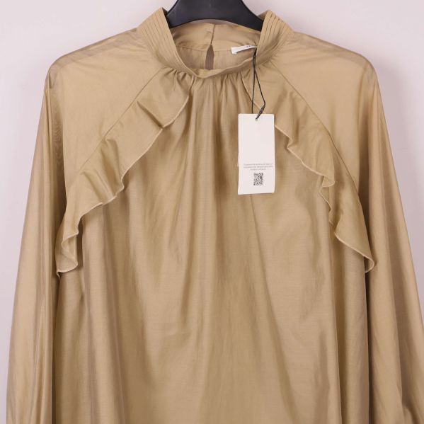 Närbild framtill på beige blus med rysch runt axlarna
