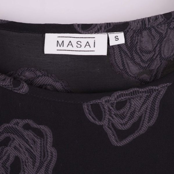 Närbild på Masai-logga samt storlek S i nacken på blusen