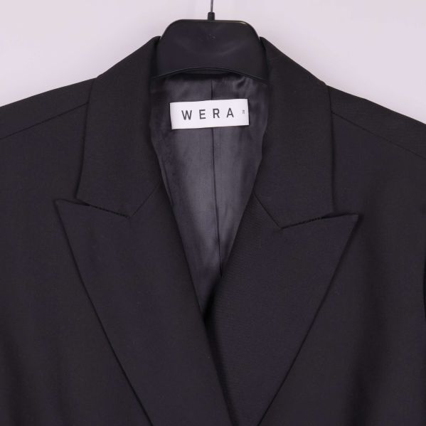 Närbild på krage och WERA-märke på svart blazer