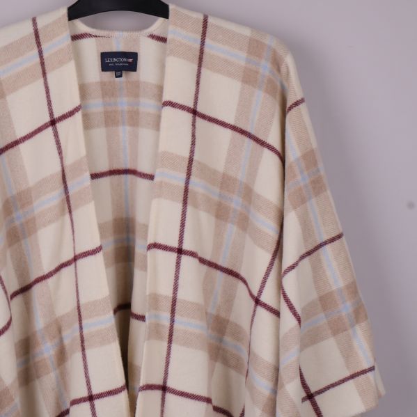 Närbild på ponchons rutiga mönster i beige och börd