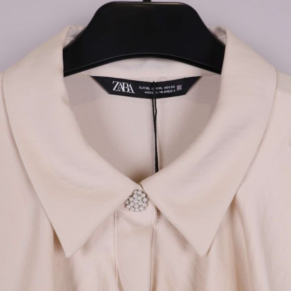 Närbild på krage med pärlknapp på beige blus