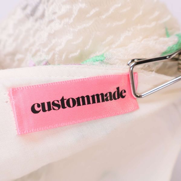 Rosa etikett med custommade-logotyp i svart text