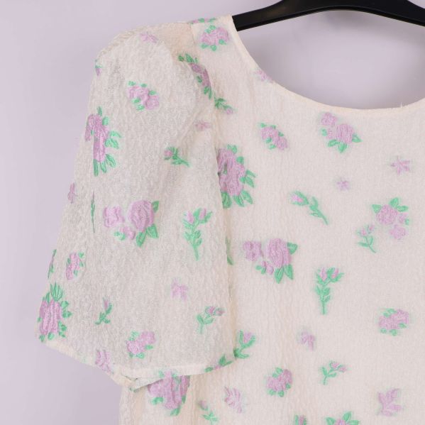 Närbild på puffärm och broderade blommor i lila och grönt