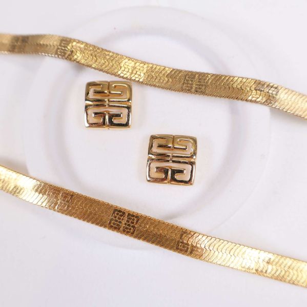 Närbild på örhängen och halsband i guldton med logotypmönster