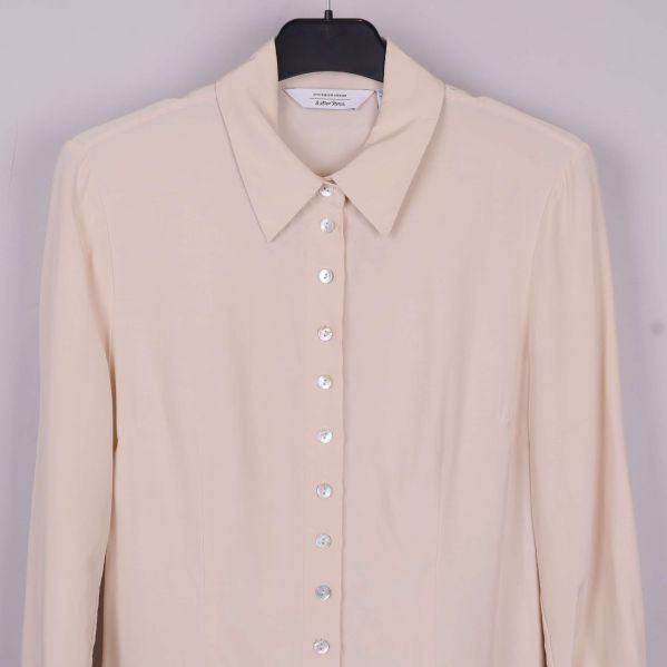 Övre del av beige blus med klassisk krage och knappslå
