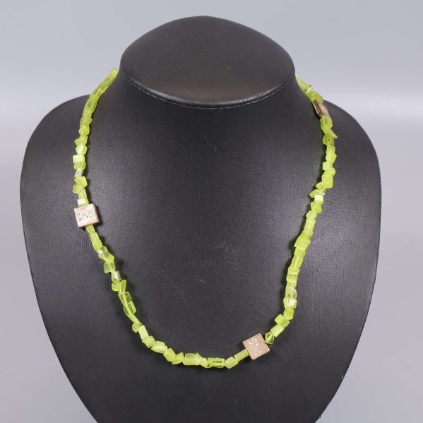 Närbild på limegrönt halsband med gulddetaljer runt displayen