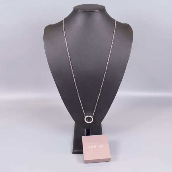 Långt silverfärgat halsband med cirkelformat hänge på ställning