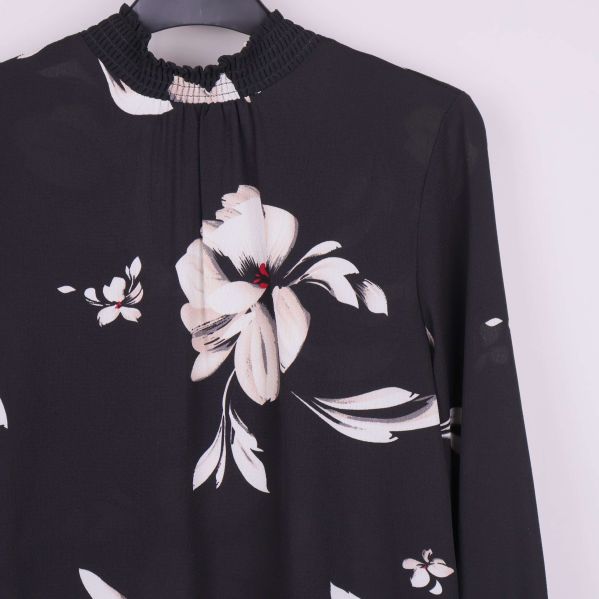 Detaljbild av blomtryck och hög halsringning på blus